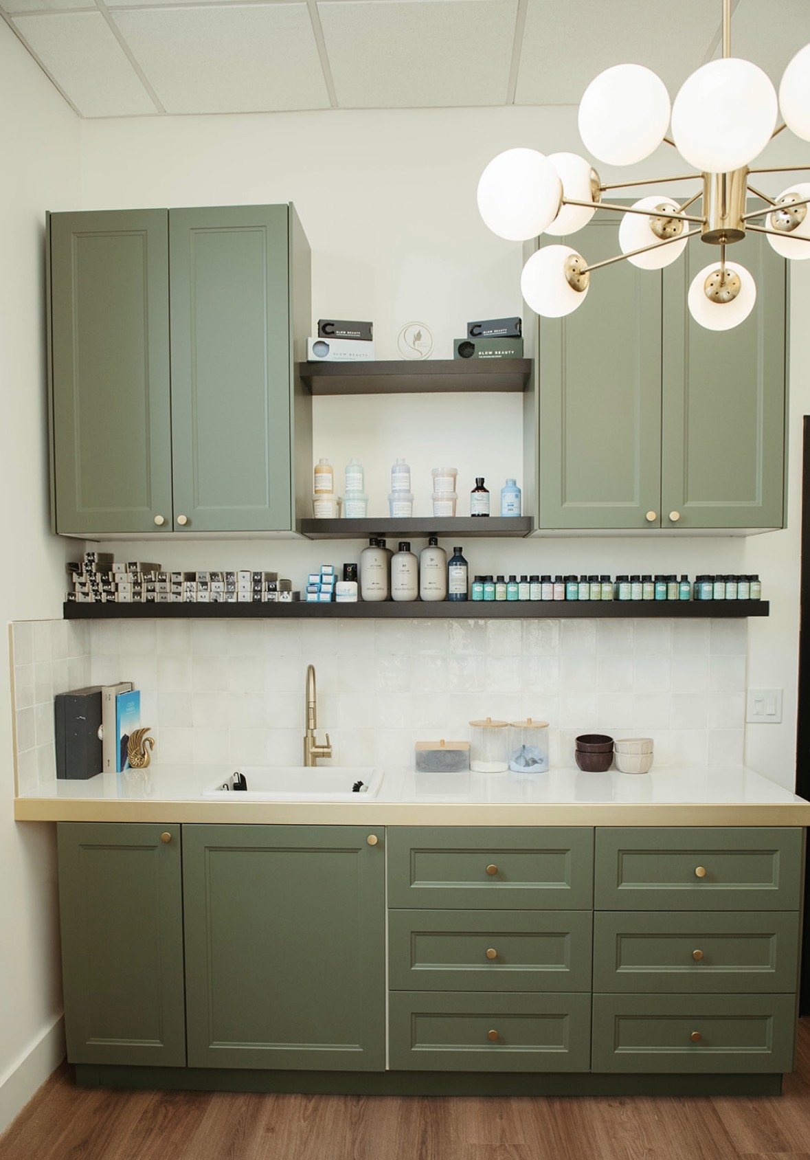 Olive green cabinetry, color bar and brass globe chandelier